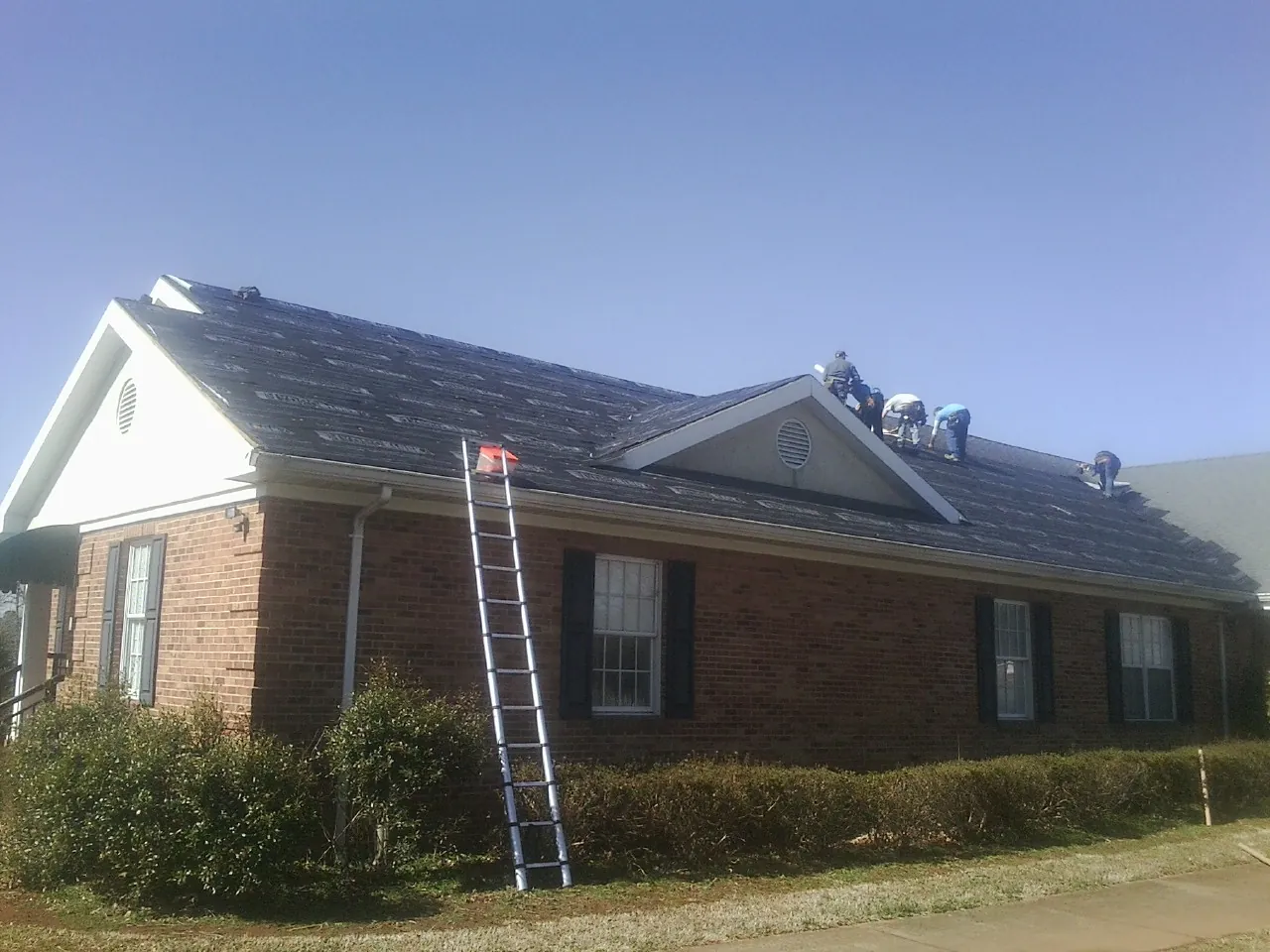 Crew tearing shingles off a brick ranch roof with a ladder set — Emergency Roof Repair work by our crew in Eagan