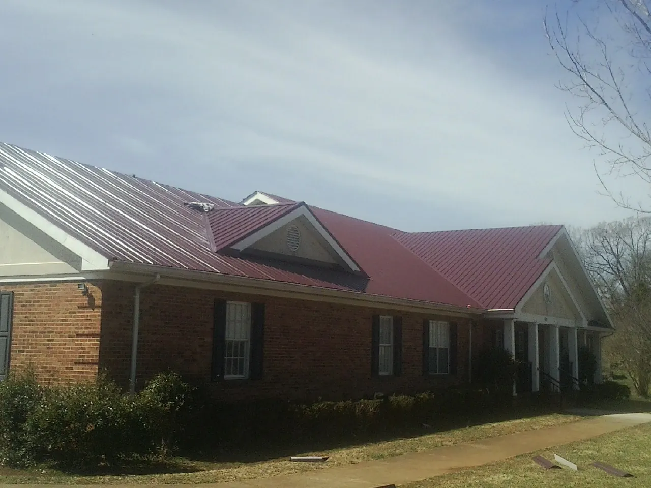 Red metal roof with gabled entries on a long brick building, from a Hail Damage Roof Repair job in Eagan