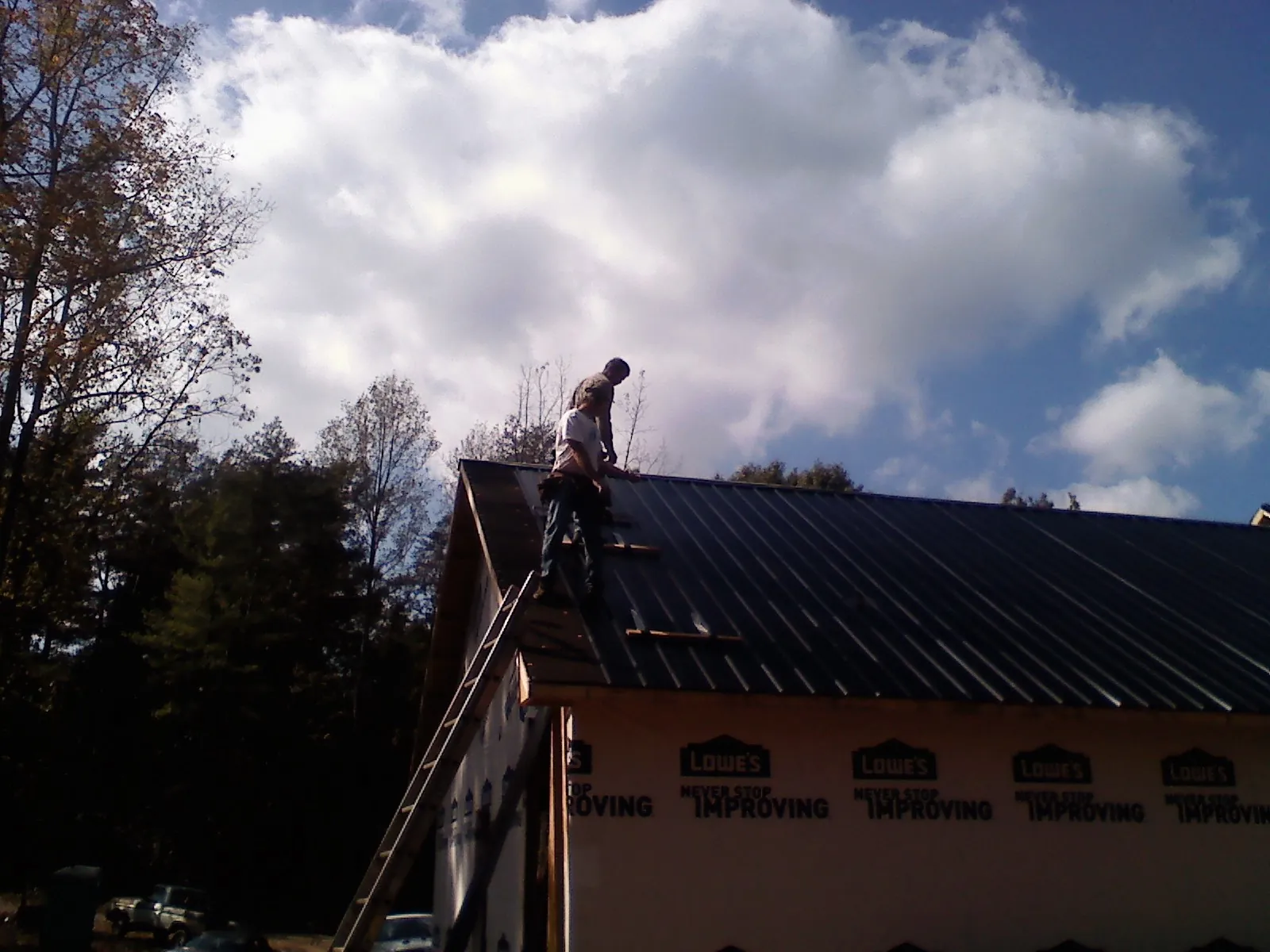 Roofer fastening dark metal panels high against a cloudy sky, from a Roof Inspection job in Eagan