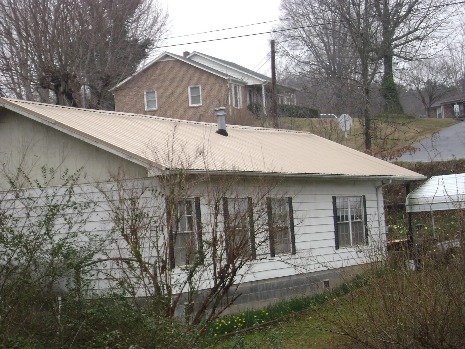 Tan metal roof on a white sided house set into a hillside — Commercial Roofing by Roofing Brothers in Eagan